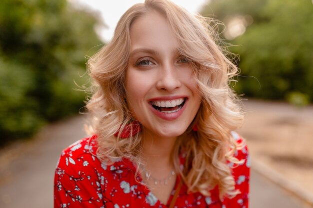 Portrait de jolie femme souriante blonde élégante en chemisier rouge tenue de mode d'été portant des boucles d'oreilles souriant