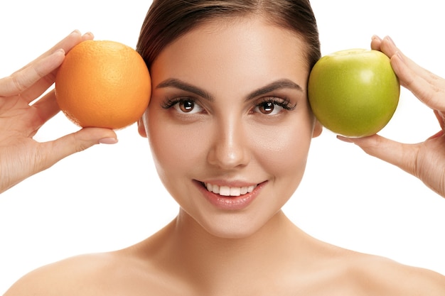 Portrait de jolie femme souriante caucasienne isolée sur blanc tenant une pomme verte et une orange