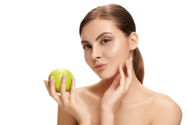 Le portrait de jolie femme souriante caucasienne isolée sur fond de studio blanc avec des fruits de pomme verte. Le concept de beauté, soins, peau, traitement, santé, spa, cosmétique et publicité