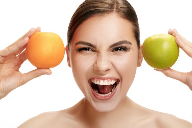 Le portrait d'une jolie femme souriante caucasienne isolée sur fond de studio blanc avec pomme verte et fruits orange