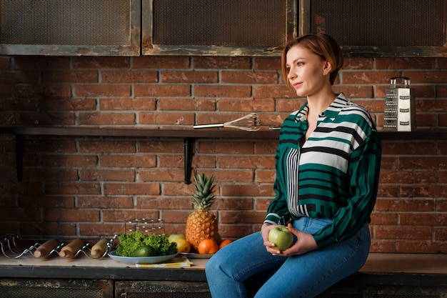 Portrait d&#39;une jolie femme tenant la pomme en position assise sur la table de la cuisine.