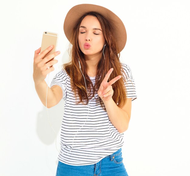 Portrait d'une jolie femme en vêtements d'été hipster prenant un selfie isolé sur mur blanc