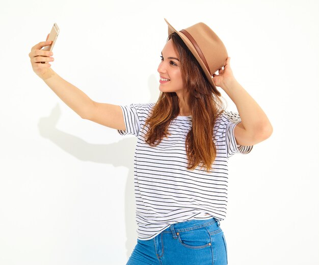 Portrait d'une jolie femme en vêtements d'été hipster prenant un selfie isolé sur mur blanc