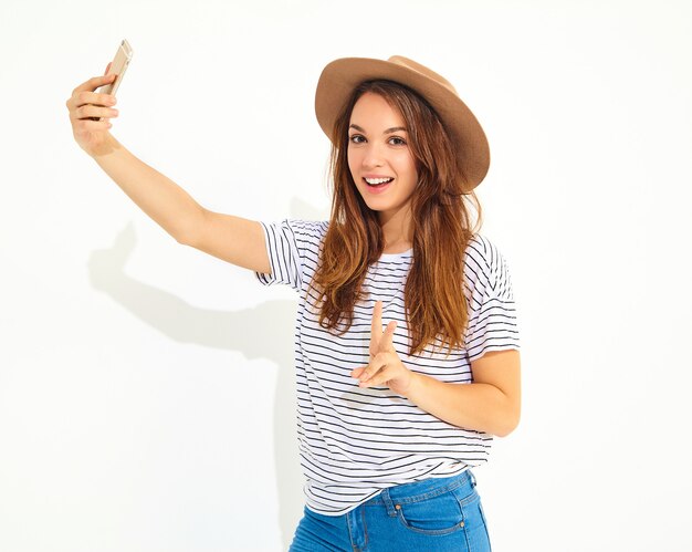 Portrait d'une jolie femme en vêtements d'été hipster prenant un selfie isolé sur mur blanc