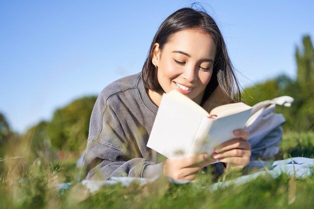 Portrait d'une jolie fille coréenne lisant dans le parc allongé sur l'herbe se relaxant avec son livre préféré à han