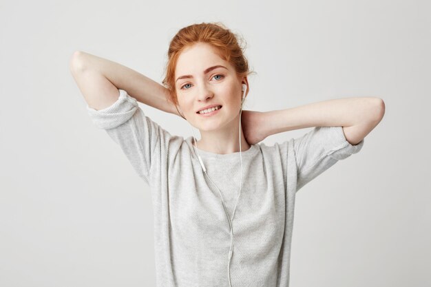 Portrait de jolie fille foxy, écouter de la musique dans les écouteurs en souriant. Mains derrière la tête.