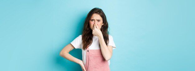 Portrait de jolie fille gênée fermer le nez et froncer les sourcils de mauvaise odeur sentant quelque chose de puanteur s