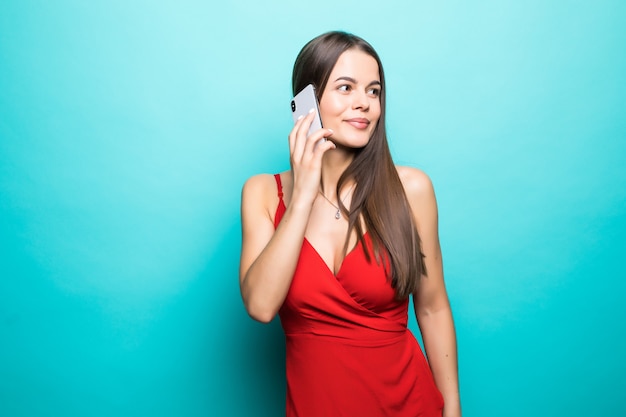Portrait d'une jolie fille joyeuse en robe parler sur téléphone mobile isolé sur mur bleu
