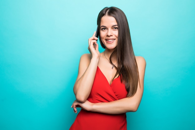 Portrait d'une jolie fille joyeuse en robe rouge parlant au téléphone mobile isolé sur mur bleu