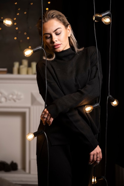 Portrait d'une jolie fille en pull noir debout près des lampes.