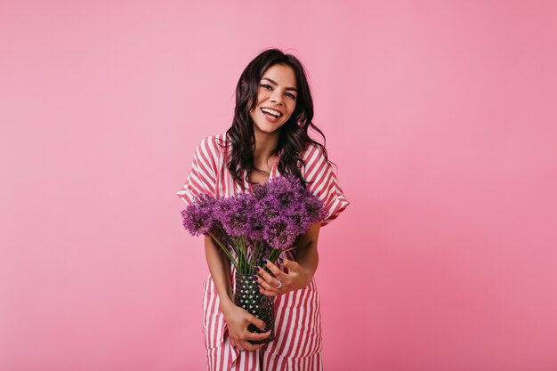 Portrait de jolie fille avec un sourire charmant. Dame en haut rayé bénéficiant de fleurs.