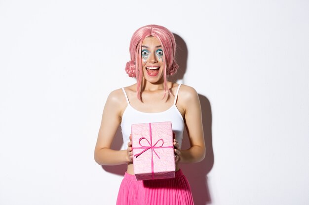 Portrait de jolie fille surprise à la recherche excitée, recevoir un cadeau pour anniversaire, portant une perruque rose, debout.
