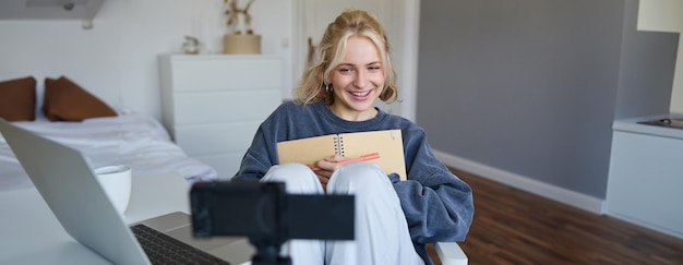 Photo gratuite portrait d'une jolie jeune créatrice de contenu de médias sociaux souriante qui enregistre une vidéo sur une caméra numérique et