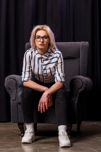 Portrait d&#39;une jolie jeune femme blonde assise sur un fauteuil en regardant la caméra