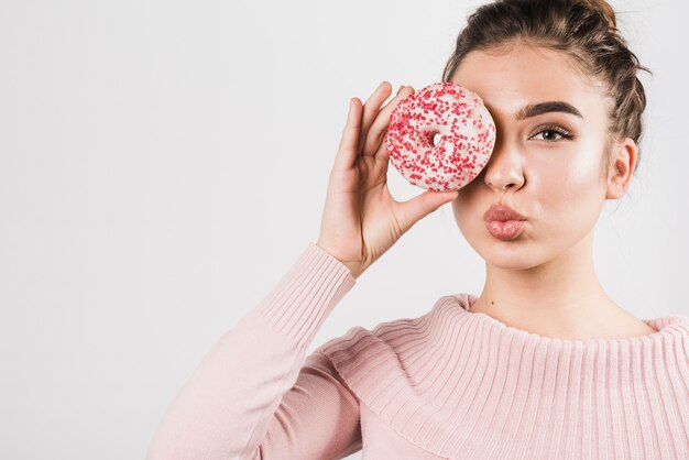 Portrait de jolie jeune femme couvrant ses yeux avec des beignets