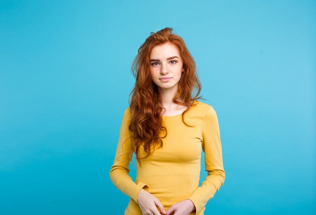 Portrait d&#39;une jolie jeune femme gingembre avec un visage tendre et terne qui croise les bras en regardant la caméra. Isolé sur fond bleu pastel. Espace de copie.