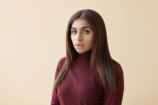 Portrait de jolie jeune femme métisse aux cheveux longs habillés en pull à col roulé marron debout