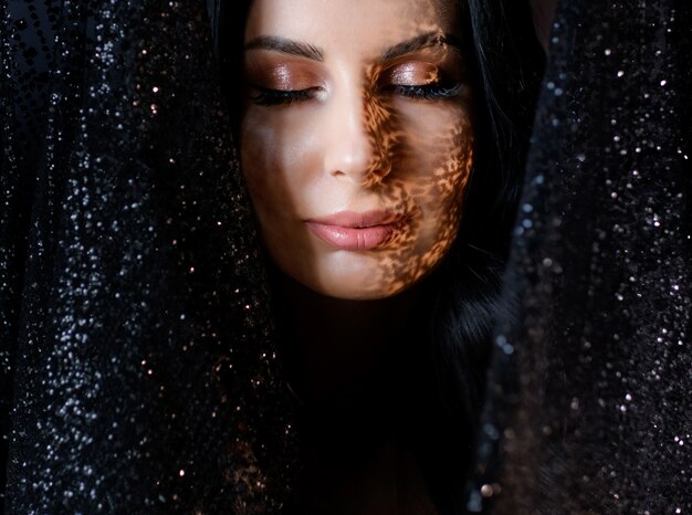 Portrait de jolie jeune fille avec un maquillage tendre et une ombre sur le visage entourée de dentelle scintillante noire