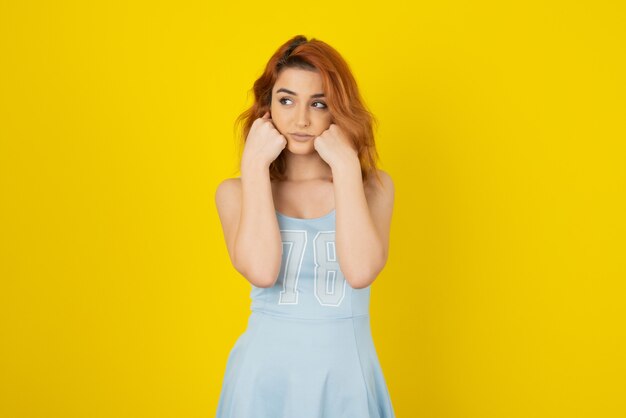 Portrait de jolie jeune fille sur le mur jaune tout en détournant les yeux