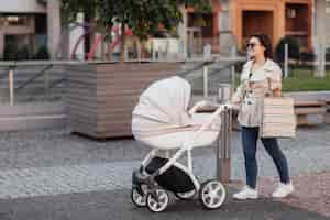 Photo gratuite portrait d'une jolie mère avec un forfait shopping marchant avec une poussette dans le centre-ville