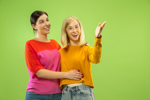 Portrait de jolies filles charmantes dans des tenues décontractées isolées sur un espace vert. Deux modèles féminins comme copines ou lesbiennes