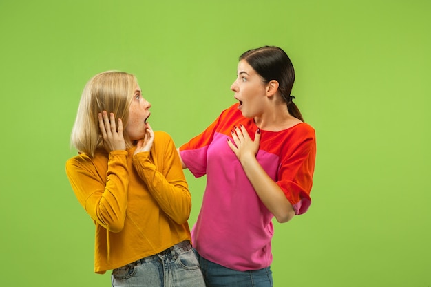 Portrait de jolies filles charmantes dans des tenues décontractées isolées sur fond de studio vert. Deux modèles féminins en copines ou lesbiennes. Concept de LGBT, égalité, émotions humaines, amour, relation.