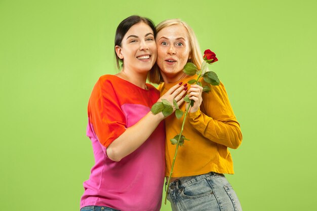 Portrait de jolies filles charmantes dans des tenues décontractées isolées sur fond de studio vert. Deux modèles féminins en copines ou lesbiennes. Concept de LGBT, égalité, émotions humaines, amour, relation.