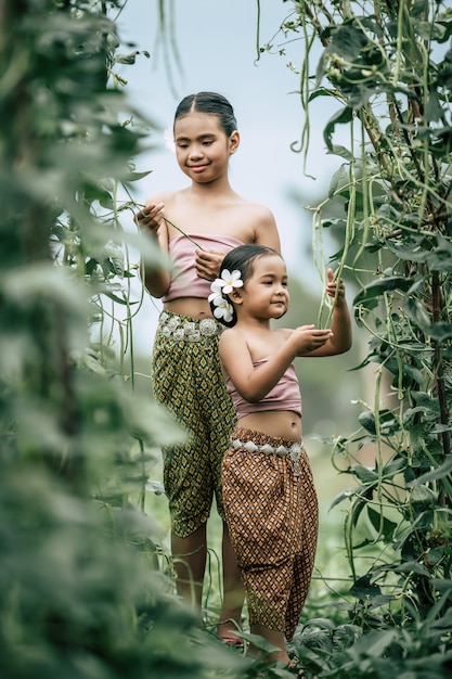 Photo gratuite portrait de jolies filles en costume traditionnel thaïlandais et mettre une fleur blanche sur son oreille, debout dans la cour de l'usine de haricots longs, elles sourient de bonheur