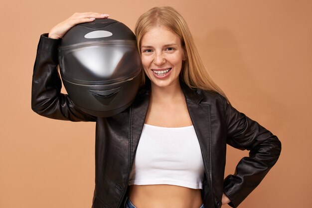 Portrait de joyeuse jeune femme avec des accolades de dents et de longs cheveux raides posant isolé en veste de cuir noir