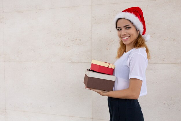 Portrait de joyeuse jeune femme en bonnet de noel avec des coffrets cadeaux