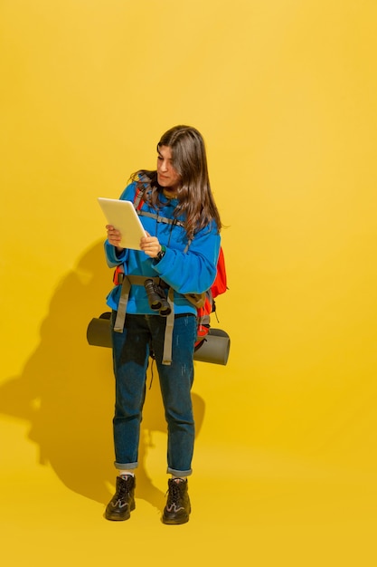 Portrait d'une joyeuse jeune fille touristique caucasienne avec sac et jumelles isolé sur fond jaune studio.