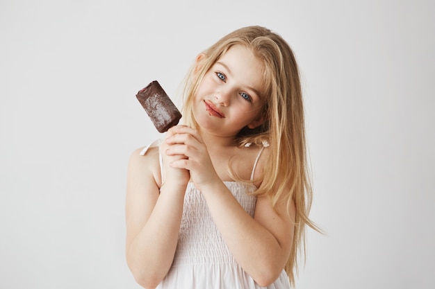 portrait de joyeuse petite fille aux yeux bleus et cheveux clairs appréciant sa glace au chocolat reste sur son visage. Enfance heureuse et insouciante