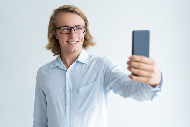 Portrait de joyeux jeune étudiant prenant selfie avec smartphone