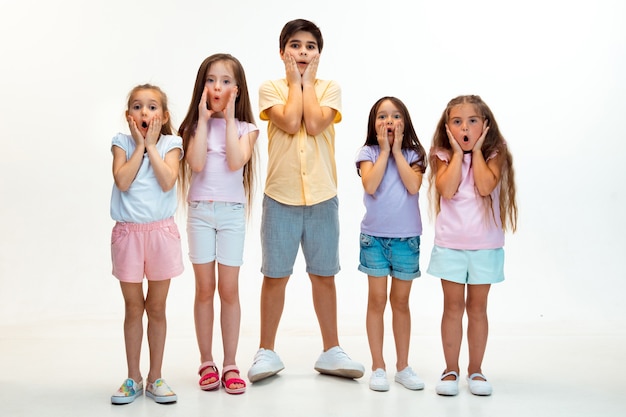 Le portrait de joyeux petits enfants mignons garçon et filles dans des vêtements décontractés élégants à l'avant contre le mur blanc du studio