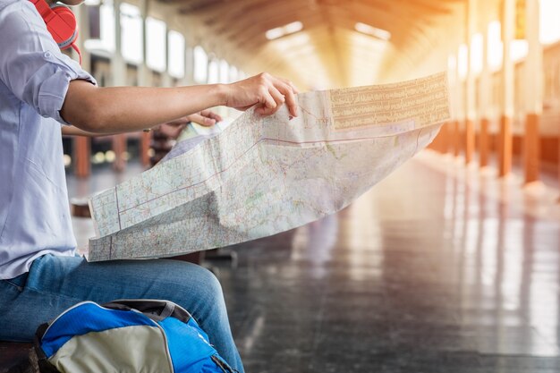 Le portrait latéral d&#39;un jeune homme voyageur assis avec la carte choisit où voyager et sac en attente de train, filtre vintage tonifié