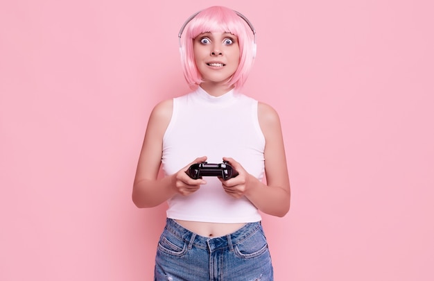 Portrait de magnifique fille heureuse gamer aux cheveux roses, jouer à des jeux vidéo à l'aide de joystick sur coloré en studio