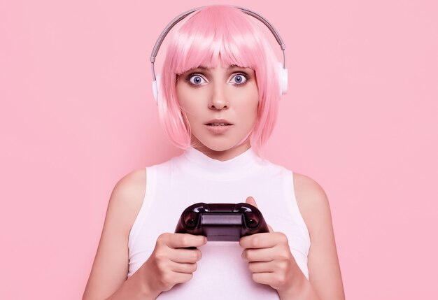 Portrait de magnifique fille heureuse gamer aux cheveux roses, jouer à des jeux vidéo à l'aide de joystick sur coloré en studio