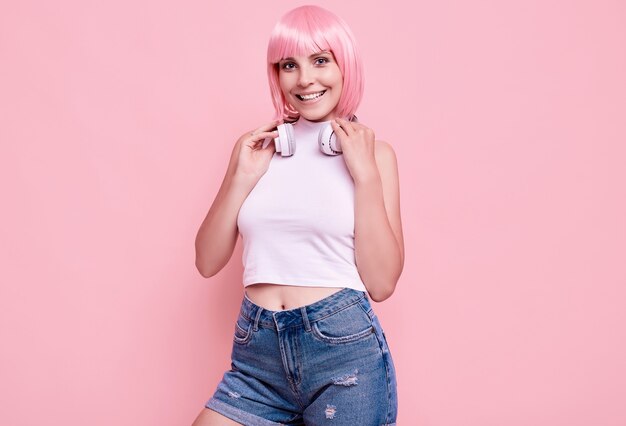 Portrait de magnifique fille hipster lumineux aux cheveux roses aime la musique dans les écouteurs sur coloré