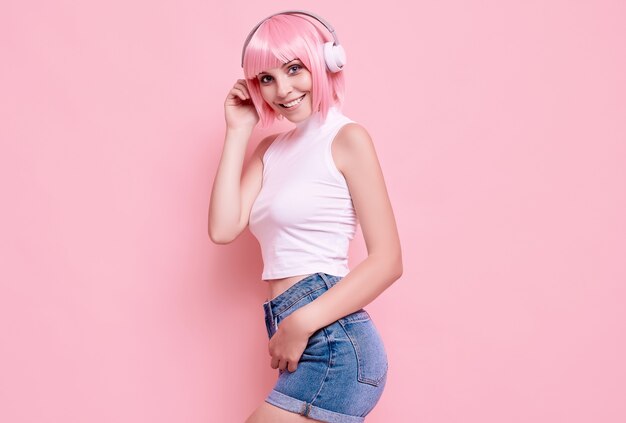 Portrait de magnifique fille hipster lumineux aux cheveux roses aime la musique dans les écouteurs sur coloré