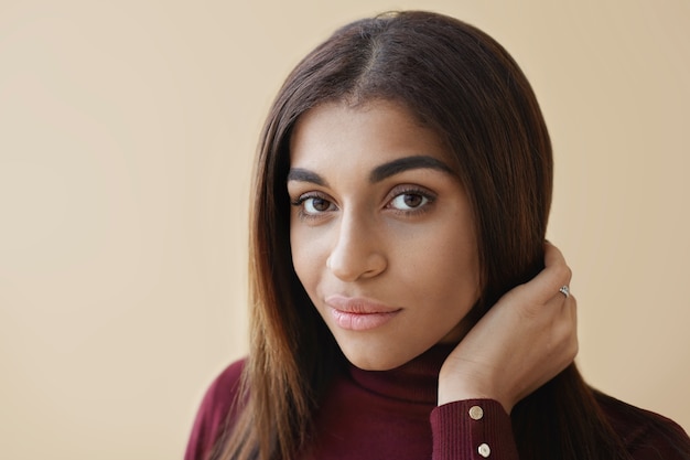 Portrait de magnifique jeune modèle féminin à la peau sombre avec de luxueux cheveux longs en bonne santé posant, shampooing publicitaire ou produits de beauté de soins capillaires, à la recherche d'un sourire charmant