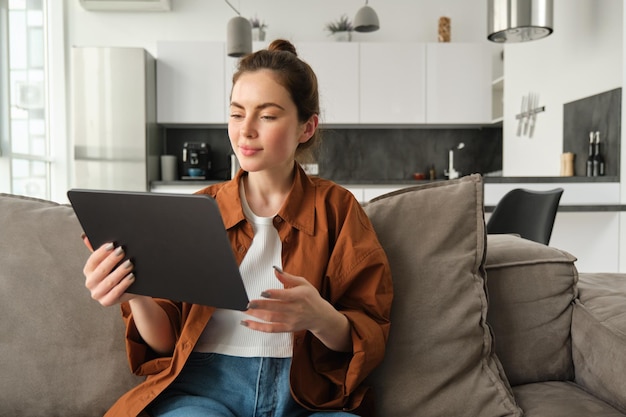 Photo gratuite portrait d'une mannequin lisant un livre électronique sur une tablette numérique et regardant une série télévisée sur son gadget