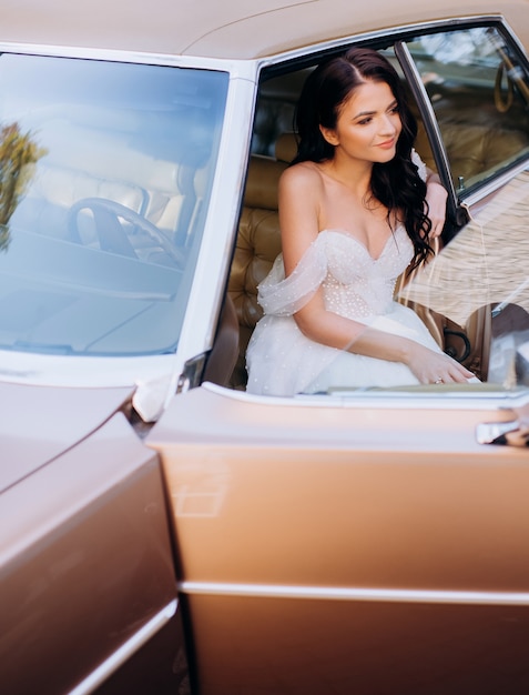 Portrait de mariée brune assise sur le siège avant d'une voiture rétro rose