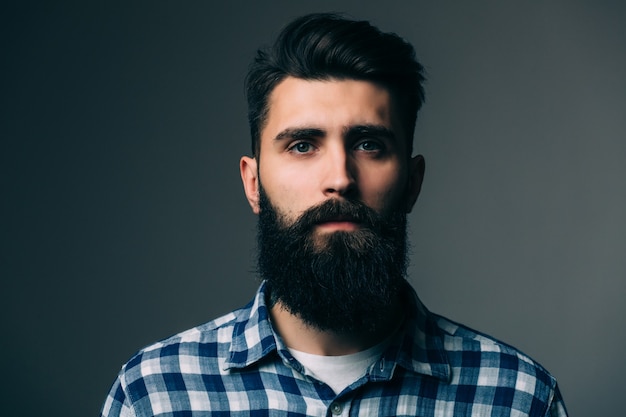 Portrait de masculinité. Portrait de beau jeune homme barbu debout contre un mur gris