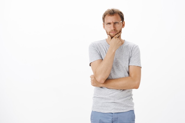 Portrait d'un mec caucasien douteux plissant les yeux en se frottant le menton et en regardant concentré tout en prenant une décision en hésitant et en se sentant douteux de la gestion de la pensée d'entreprise