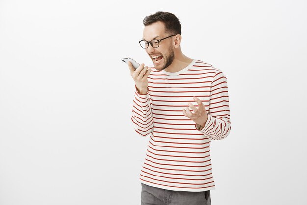 Portrait de mec en colère énervé avec des poils dans des lunettes noires, criant au smartphone et secouant le poing