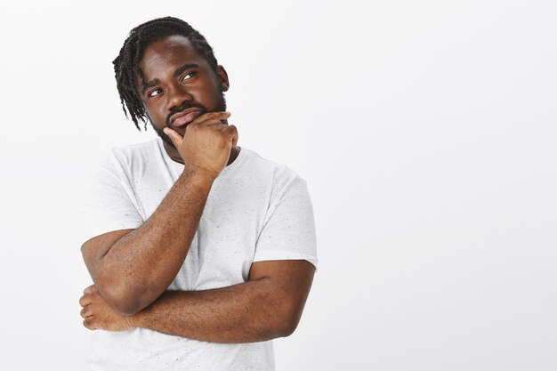 Portrait de mec concentré avec des tresses posant contre le mur blanc