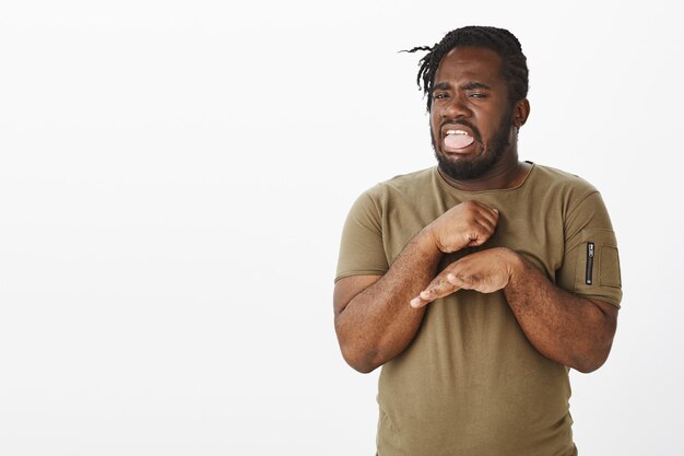 Portrait de mec dégoûté dans un t-shirt marron posant contre le mur blanc