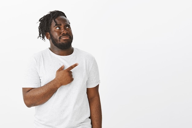 Portrait de mec douteux avec des tresses posant contre le mur blanc