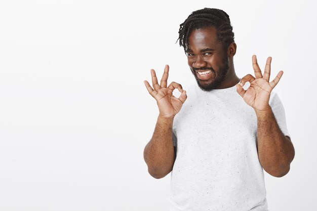 Portrait de mec heureux avec des tresses posant contre le mur blanc