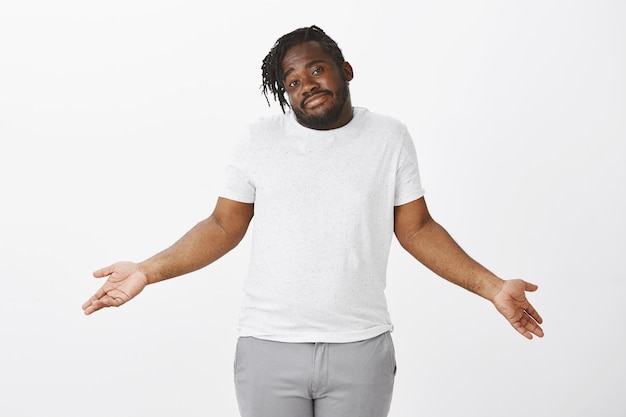 Portrait de mec insouciant avec des tresses posant contre le mur blanc